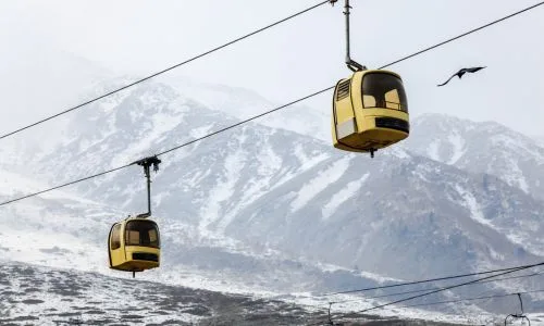 Yellow Gulmarg gondola cabin gliding above snow-covered slopes and pine trees
