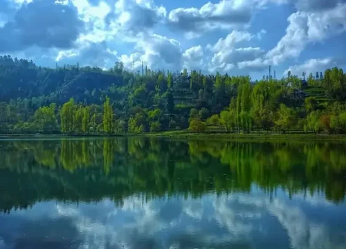 A calm blue alpine lake hidden in dense pine forests near Yusmarg.